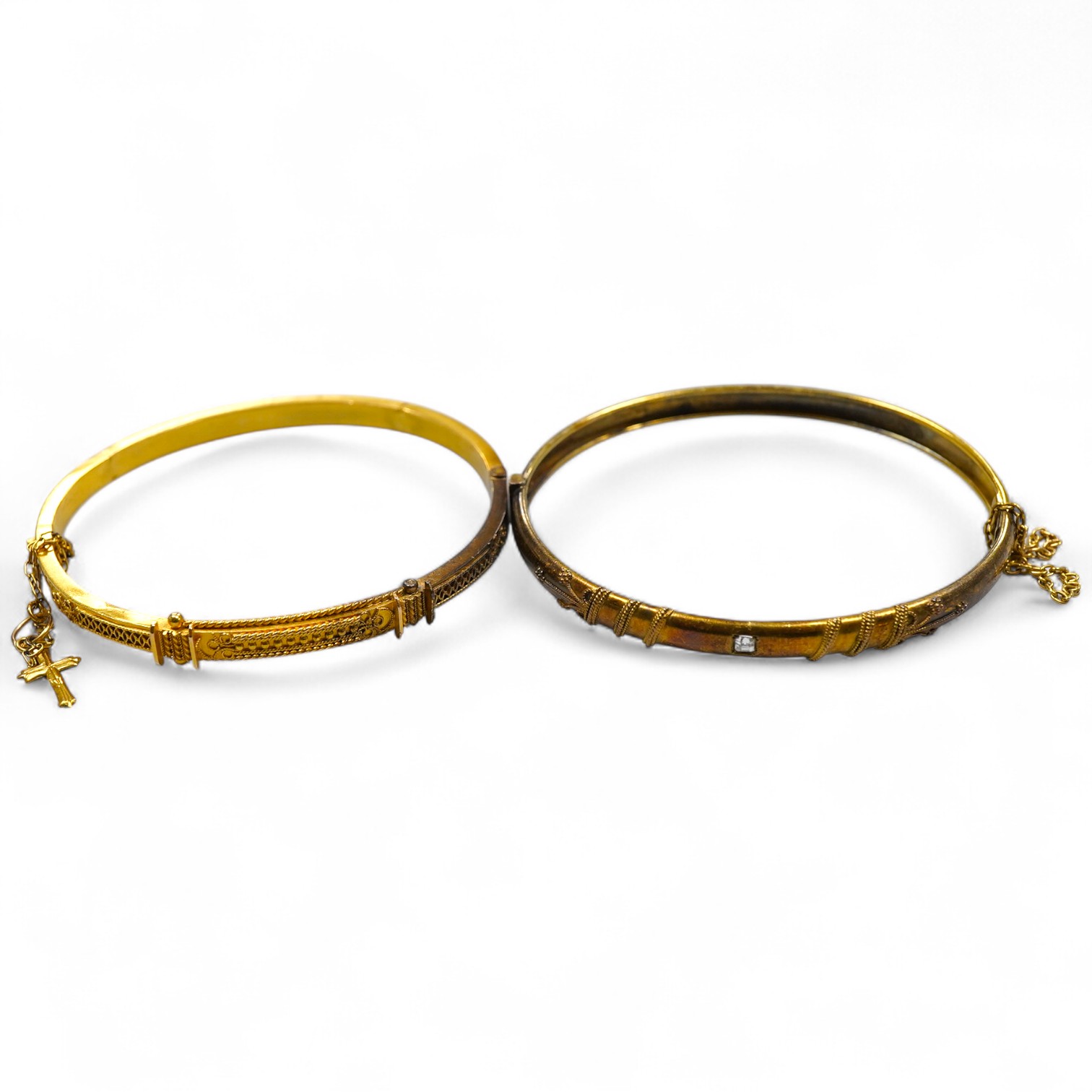 Two Victorian gold bangles, late 19th century, each of hinged design, with rope twist decoration, one later set with a carré-cut diamond, the other suspending a cross from a safety chain, inner circumferences approximate
